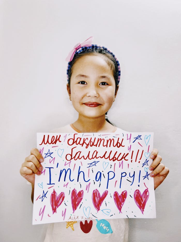 Smiling child in Talgar holds a vibrant sign expressing happiness, written in multiple languages.