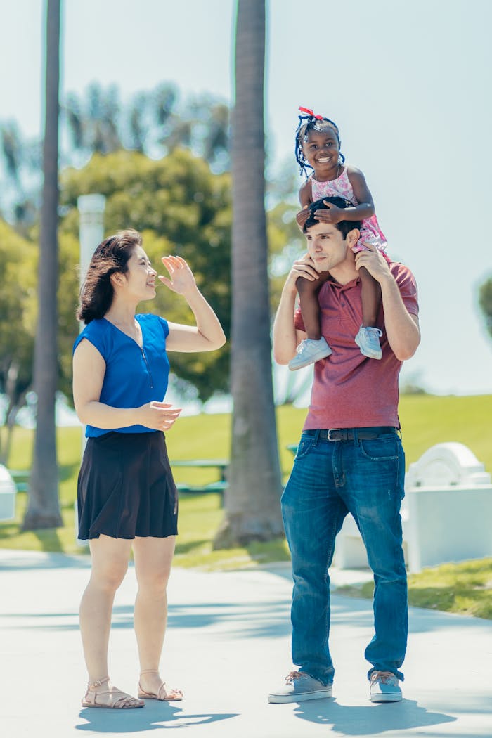 Multicultural family having fun outdoors. Father carrying daughter, mother smiling.