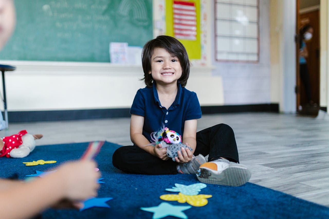 A cheerful child sitting on the floor, playing with a toy in a classroom environment.